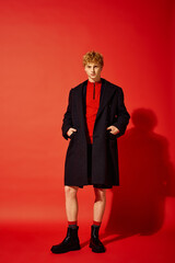 A stylish man stands confidently against a bright red backdrop, wearing a cozy red pullover beneath...