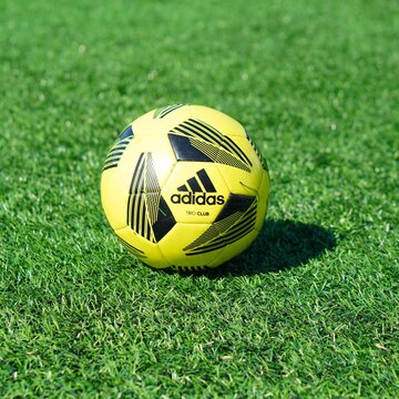 Yellow Adidas soccer ball resting on lush green grass in the glorious sunlight.