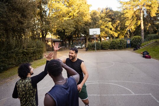 A group of basketball players smiling and high-fiving each other after a game on an outdoor park court surrounded by lush trees and a peaceful setting