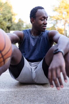A basketball player rests on the court while holding the ball, surrounded by trees and basking in the sunlight in a quiet park
