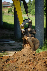 Mini excavator digs a narrow trench in soil for laying communications close-up. Mini bucket of crawler machine. Earthworks with heavy special equipment. Digging machinery works at construction site