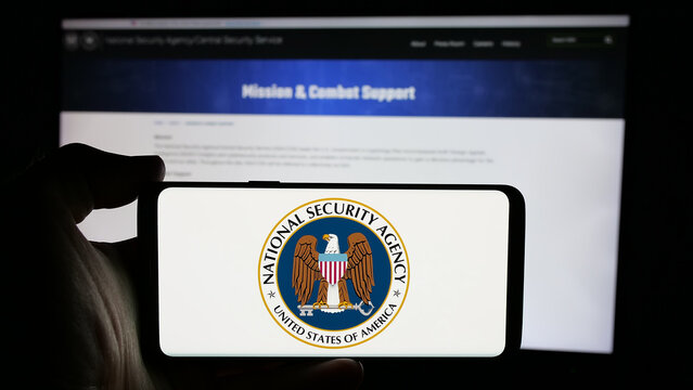 Stuttgart, Germany - 10-28-2024: Person holding cellphone with logo of National Security Agency (NSA) on screen in front of webpage. Focus on phone display.