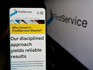 Naklejka premium Stuttgart, Germany - 10-30-2024: Person holding cellphone with web page of Canadian company FirstService Corporation on screen in front of logo. Focus on center of phone display.