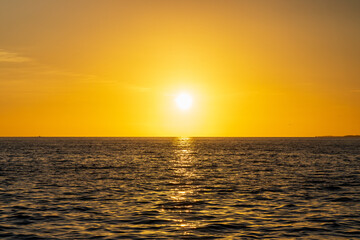 Obraz premium Golden sunset over the ocean with a silhouetted boat and a flying bird, reflecting warm light across the calm water.