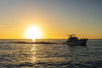 Obraz premium A motorboat glides across the ocean at sunset, with golden sunlight reflecting on the water's surface.