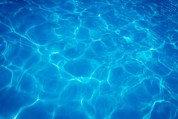 Obraz premium Clear blue swimming pool water surface with sunlight reflections creating abstract patterns and ripples, evoking a refreshing and tranquil summer vibe.