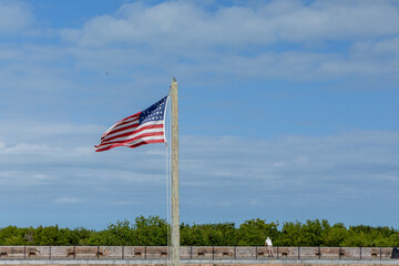 Fort courtyard with an American flag flying, brick archways, cannons, and open grassy space under a...