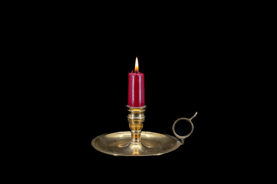 Burning red candle in a brass holder on a black background