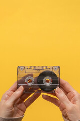 Audio cassette in female hands isolated on yellow background. Vintage audio cassette held by hand against a flat background, evoking nostalgia for retro music lovers