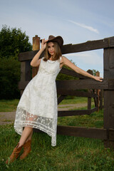 Obraz premium A young girl poses in a boho wedding dress, cowboy boots, a cowboy hat, and a denim jacket.