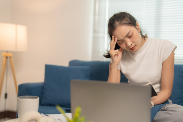 Stressed asian woman with headache working on laptop at home, tired, and overworked, suffering from...