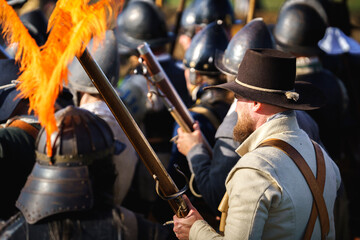 Musketeer waiting for the strike to fire. Young men in armor, costumes playing siege. Historical event. Action scene.