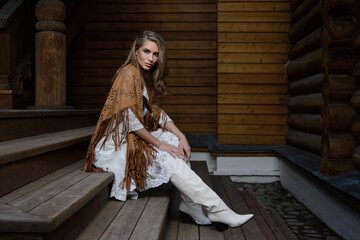 A young girl poses in a boho wedding dress, cowboy boots, a cowboy hat, and a denim jacket.