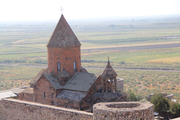 The image depicts an ancient Armenian Apostolic church featuring a conical roof, set against a...