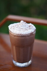 Iced chocolate drink served in a clear glass with white cream and chocolate powder on top