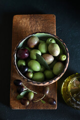 Olive fresche in una ciotola sul tagliere di legno e olio d'oliva isolato su sfondo scuro. Cibo vegetariano e sano. Direttamente sopra.