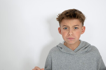 cool young 12 year old boy with grey hoody sweater posing in front of white background, having fun