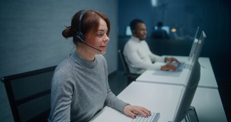Call center office: Dolly shot of female technical support specialist in headset monitoring data on PC, providing online customer support service via call. Multiethnic hotline operators team working.