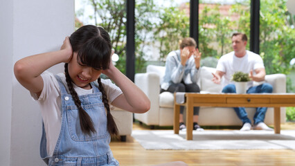 Stressed and unhappy young girl huddle in corner, cover her ears blocking sound of her parent...