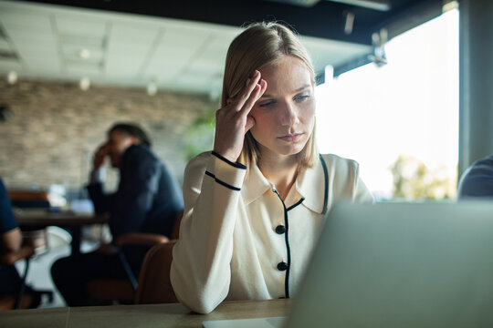 Woman looking stressed while working on laptop in office environment