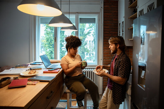 Two friends talking and eating in a cozy kitchen with laptops and notebooks