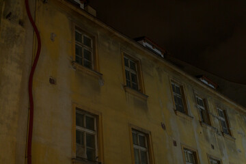 Fototapeta premium This image presents a striking nighttime view of the weathered facade of an old building, showcasing its windows and intricate wall details, all captured beautifully in low light conditions