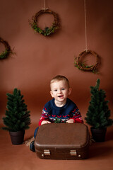 beautiful boy child 3 years old on brown background with christmas tree and an old suitcase
