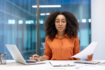 Young African American businesswoman focused on paperwork at modern office desk. Confident...