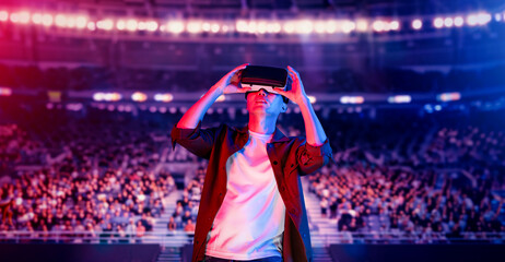 Asian man wearing VR glasses and casual cloth and surrounded with crowds cheering and sitting at arena. Gamer celebrating winning in video game while using augmented reality technology. Ingenuity.