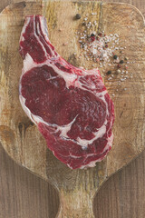 raw rib eye steak, cowboy steak, on a wooden chopping board, top view, no people,