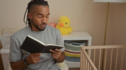 Young man with braids reading a book aloud to a baby in a cradle beside him in a cozy bedroom setting, showcasing a nurturing moment between father and child indoors.