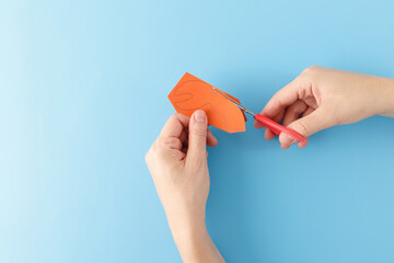 top down view hands cutting out orange paper details or cardboard pieces for the legs, claws, and eyes, part of creative process of making crab craft project. blue background, fun toy,