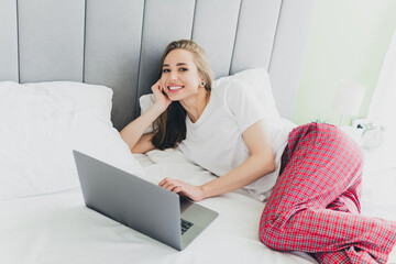Photo of cheerful dreamy lady dressed sleepwear smiling relaxing bed typing messages modern gadget indoors room home house