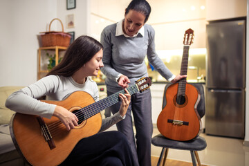 Mother and daughter playing guitar at home. A mother teaches her daughter to play the guitar.