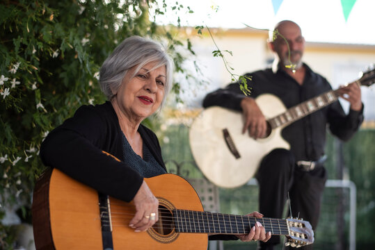 Man and woman, 65 years old, playing guitar in the Andalusian courtyard of their home