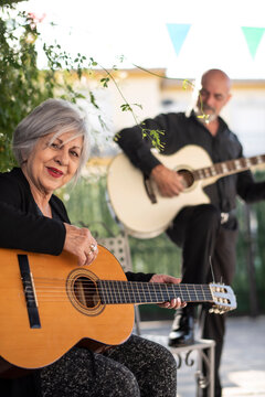 Man and woman, 65 years old, playing guitar in the Andalusian courtyard of their home