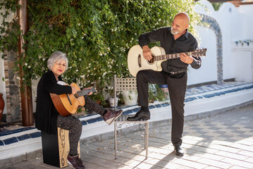 Man and woman, 65 years old, playing guitar in the Andalusian courtyard of their home