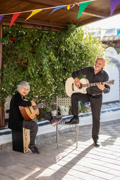 Man and woman, 65 years old, playing guitar in the Andalusian courtyard of their home
