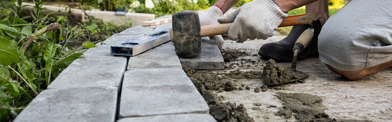 Laying paving stones on cement mortar. Banner. Laying a garden path made of tiles. Self-laying of concrete paving slabs in the courtyard of the house. do it yourself. DIY