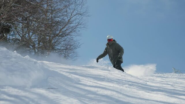 4K slow motion video of a male snowboarder snowboarding in winter making turns and jumping over snow moguls on a steep ski slope in Vermont, USA. Excitement and thrill of an extreme sport.