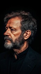 Obraz premium Profile portrait of a mature man with gray hair and beard against a dark background.