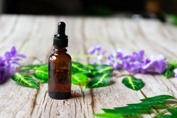 Amber vial of essential oil with a dropper, on a wooden surface, with purple flowers and leaves in the background