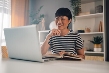 Smiling asian woman using a laptop, engaging with someone online.