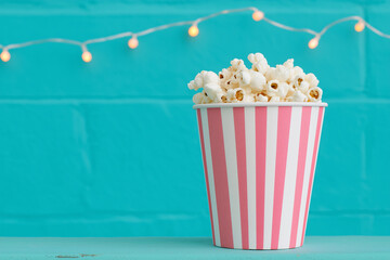 Pink and white bucket with popcorn with a blue wall and Christmas lights on a background