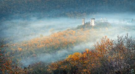 aerial view to autumn forest in morning fog and ruins of castle on the hill
