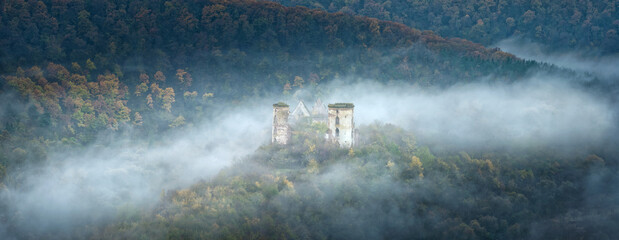 panorama of atmospheric morning with fog between hills and ruins of medieval castle in centre with copy space