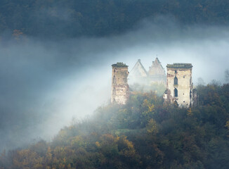 landscape with morning fog and ruins of castle and church on the hill in morning twilight