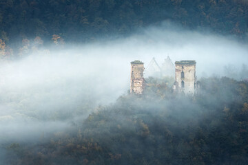 landscape in morning twilight with waves of fog around ruins of castle and church