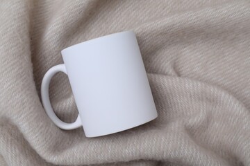 Blank white ceramic mug on beige fabric, top view. Mockup for design