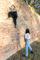 Two young women climbing and helping on a brick wall